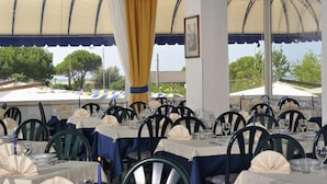 A restaurant with tables set for dining, featuring a view of trees and umbrellas outside. - Hotel Bellevue (San Michele al Tagliamento)