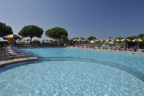 A swimming pool with clear blue water, surrounded by lounge chairs and umbrellas.