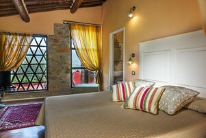 Una camera da letto con un letto grande, un muro in pietra e vista attraverso una finestra con tende.