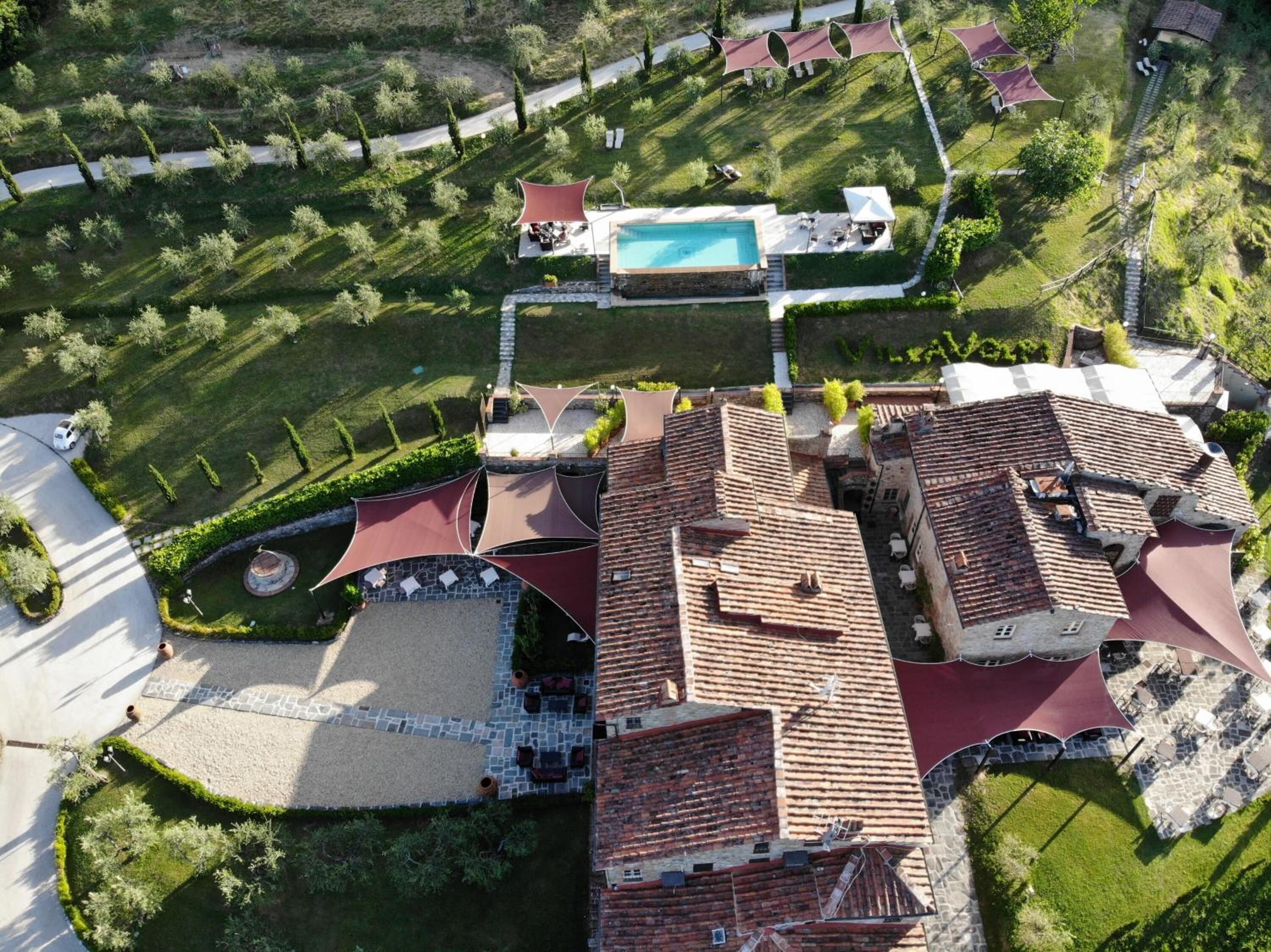 An aerial view of a residential area with a swimming pool, terraced gardens, and a paved courtyard.