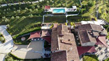 An aerial view of a residential area with a swimming pool, terraced gardens, and a paved courtyard.