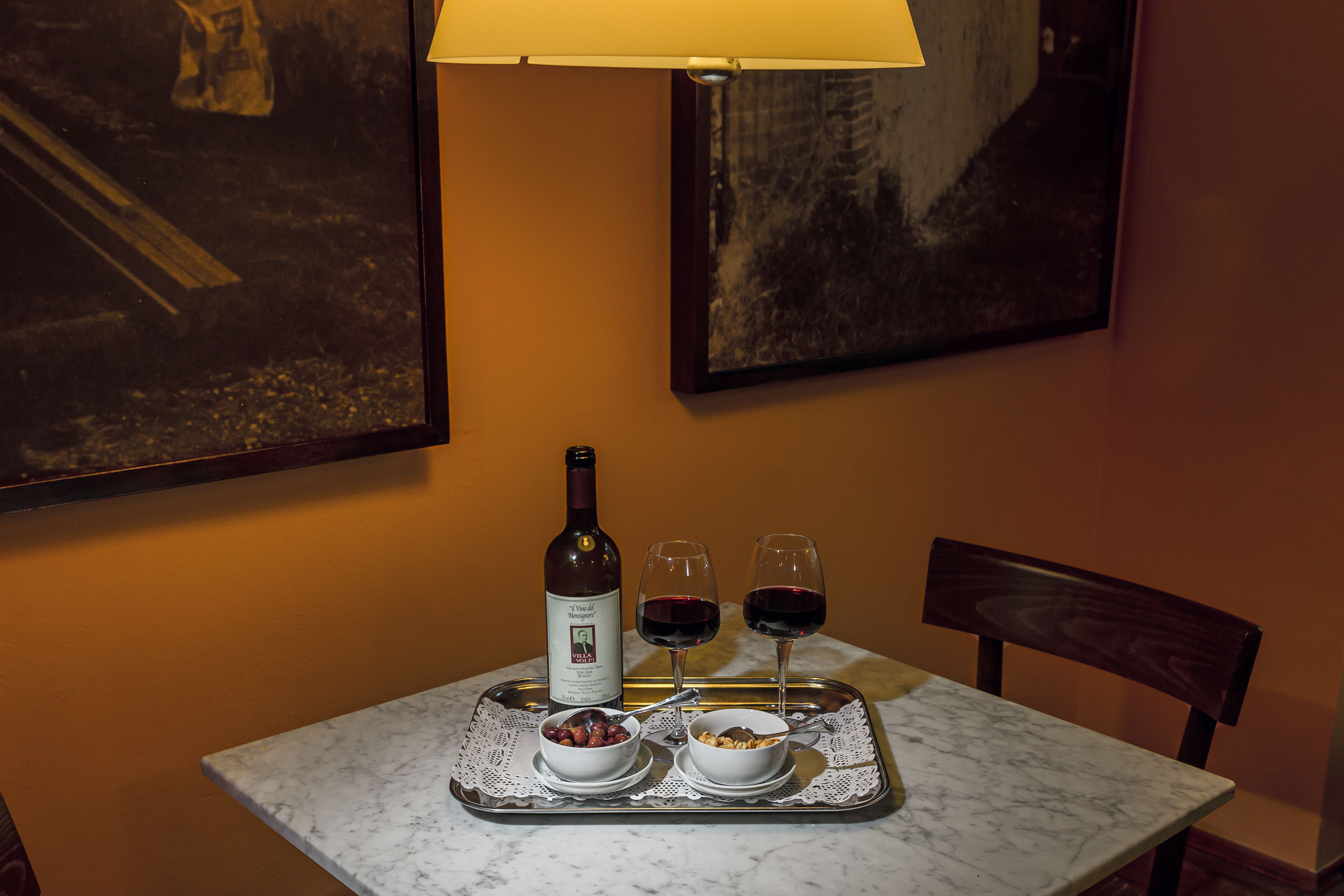 Una mesa con una bandeja que sostiene una botella de vino, dos copas de vino tinto y fuentes de comida.