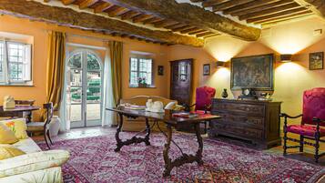 A traditional room with a wooden ceiling, a patterned rug, a sofa, a table, and a red armchair.