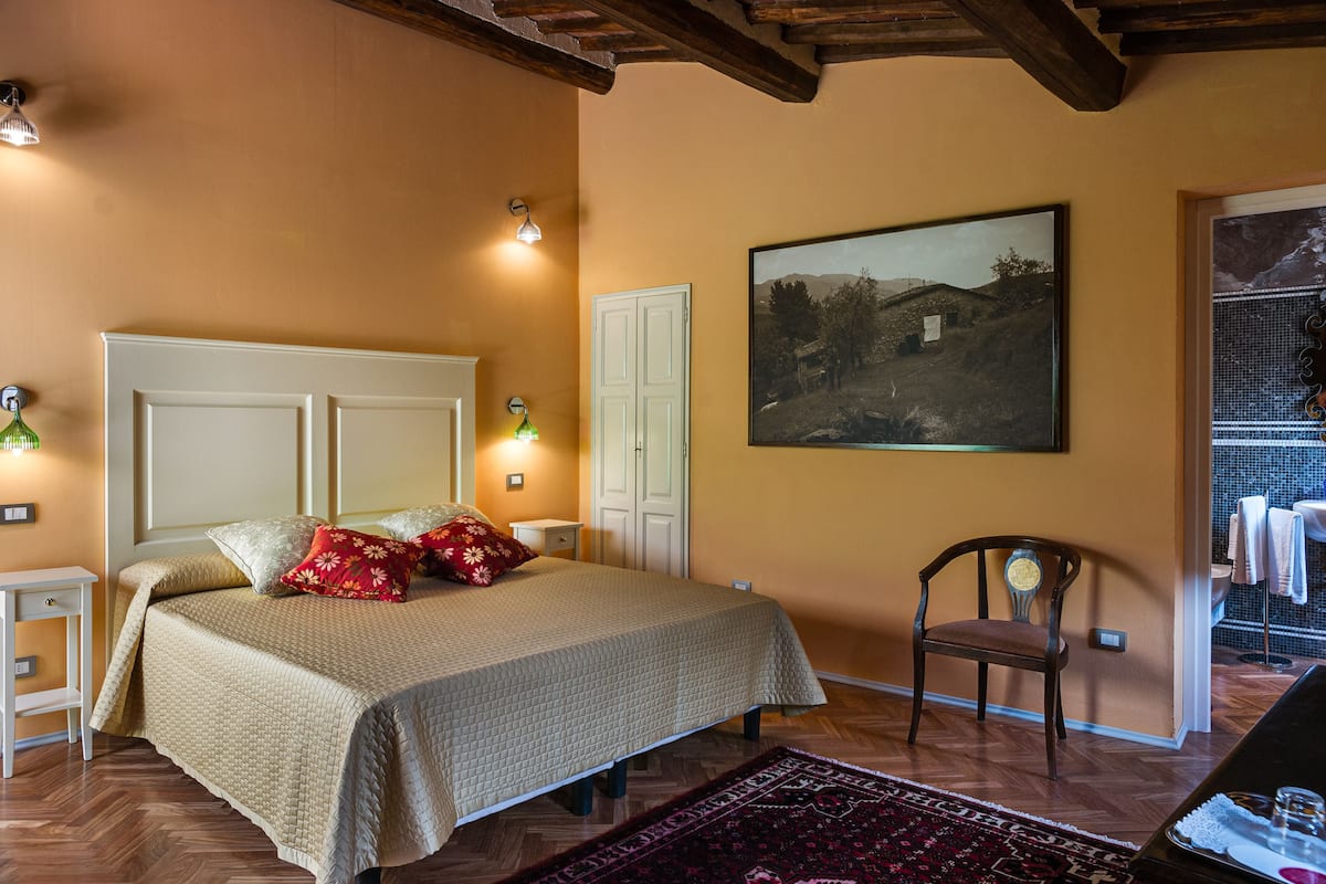 Une chambre à coucher comprenant un lit, une chaise, une table de chevet, une lampe fixée au mur et un tableau encadré.
