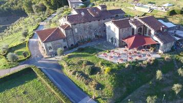 Un grand bâtiment en pierre, surmonté d’un toit de tuiles rouges, entouré d’une végétation luxuriante et agrémenté d’une piscine.