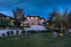 A stone building with a courtyard, surrounded by trees and well-lit pathways. - Villa Volpi (Lucca)