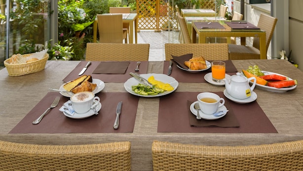 A breakfast setup with wicker chairs, a glass table, and a view of a garden. - Hotel Vittoria (Viareggio)