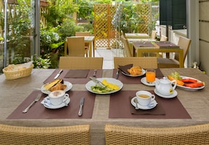 A breakfast setup with wicker chairs, a glass table, and a view of a garden. - Hotel Vittoria (Viareggio)