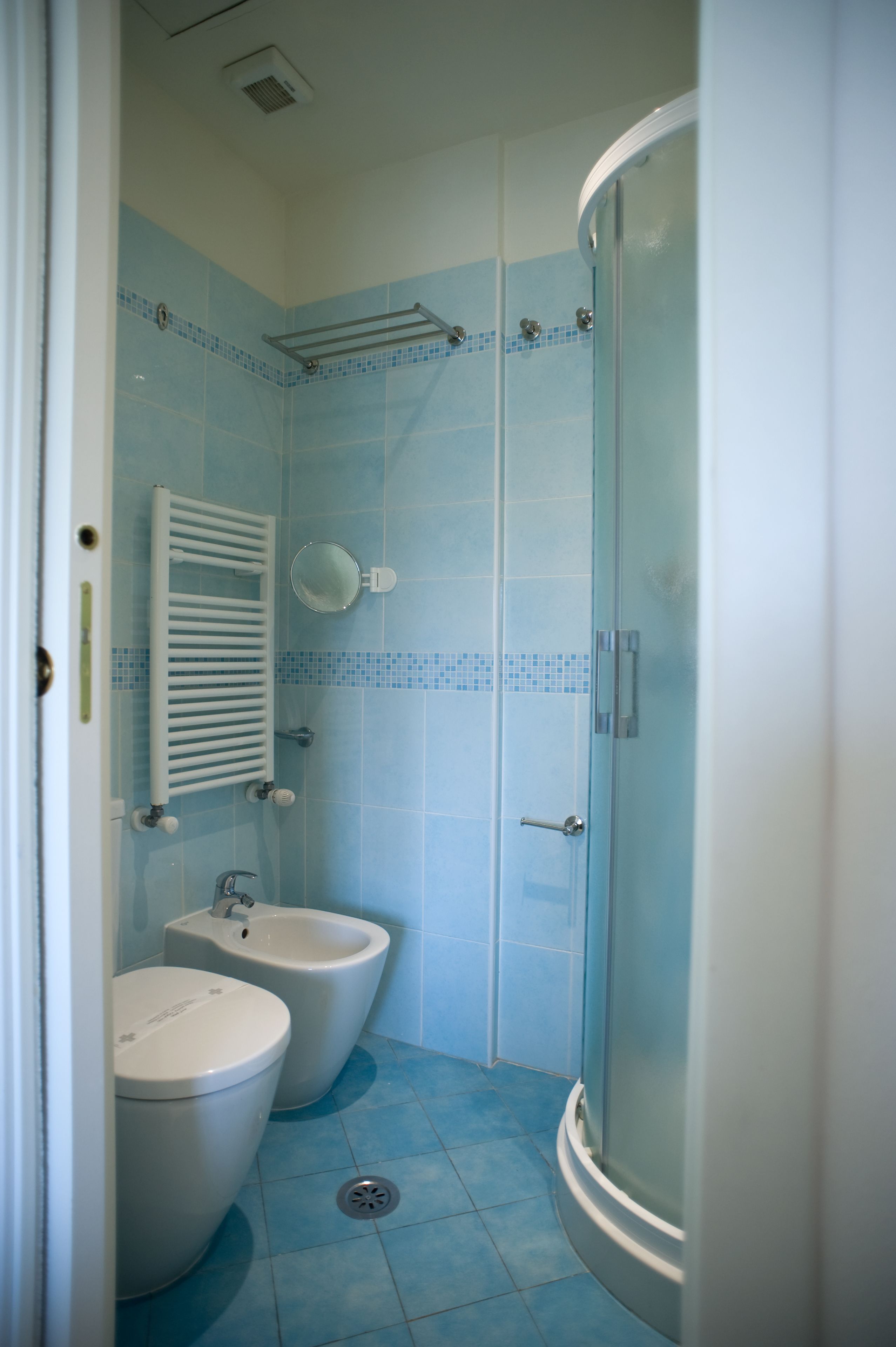 A bathroom with two toilets, a bidet, a glass shower enclosure, and a tiled floor.