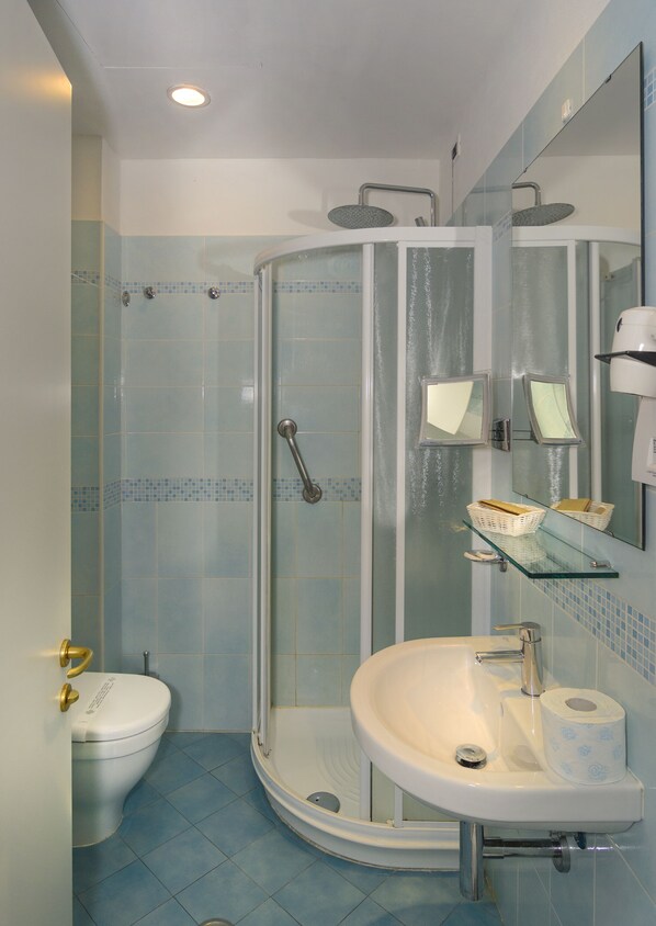 Un baño con ducha, inodoro, lavabo y un estante de vidrio con artículos de aseo.