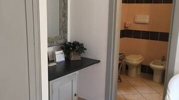 Een badkamer met een wit wastafelmeubel, een spiegel met decoratieve lijst, een potplant, een toilet en een douchetoilet.