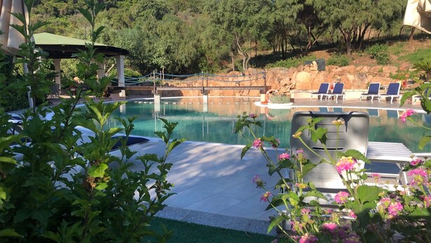 A swimming pool with lounge chairs, surrounded by greenery and a hilly landscape.