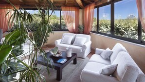 A room with a wooden ceiling, white sofas, a coffee table, and large windows with curtains.