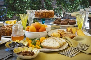 A table set with various food items and drinks, including pastries, bread, and a fruit bowl.