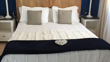 Una cama con cabecera de madera, ropa de cama blanca y una manta negra. Hay dos mesitas de noche, con lámparas y un teléfono en una de ellas.