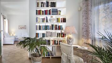 Een kamer met een grote boekenkast, een witte stoel, een lamp en een potplant.