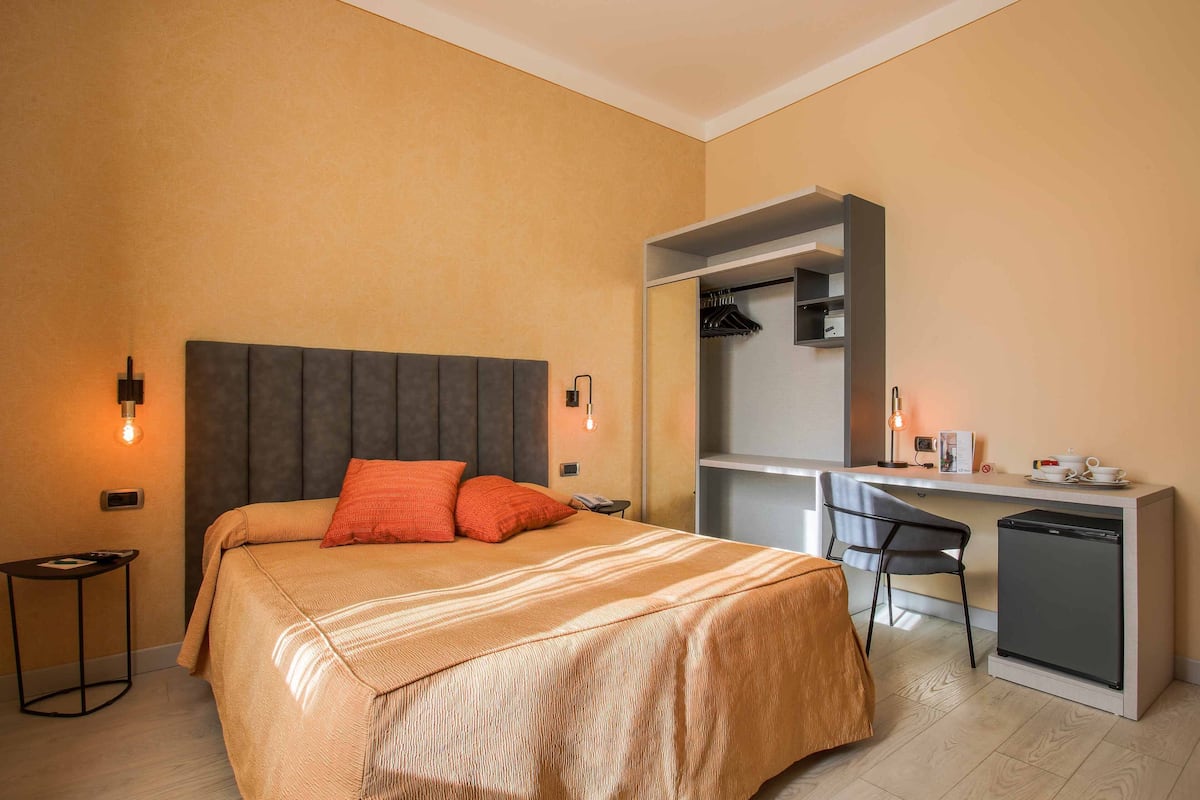 Ein Schlafzimmer mit Bett, Nachttisch, Schreibtisch, Stuhl und einem kleinen Kühlschrank.