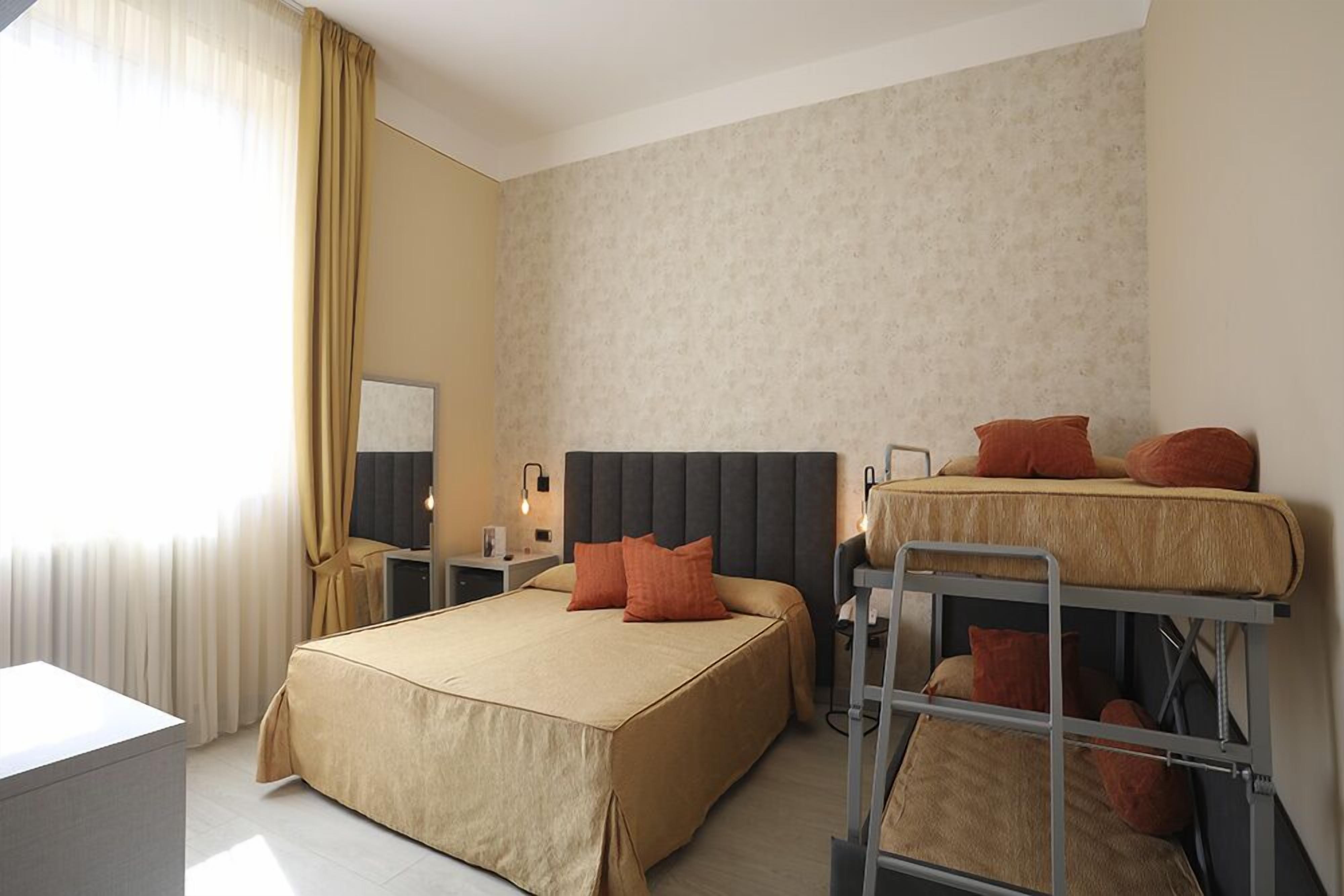 Habitación de hotel con cama individual, literas, escritorio y silla.