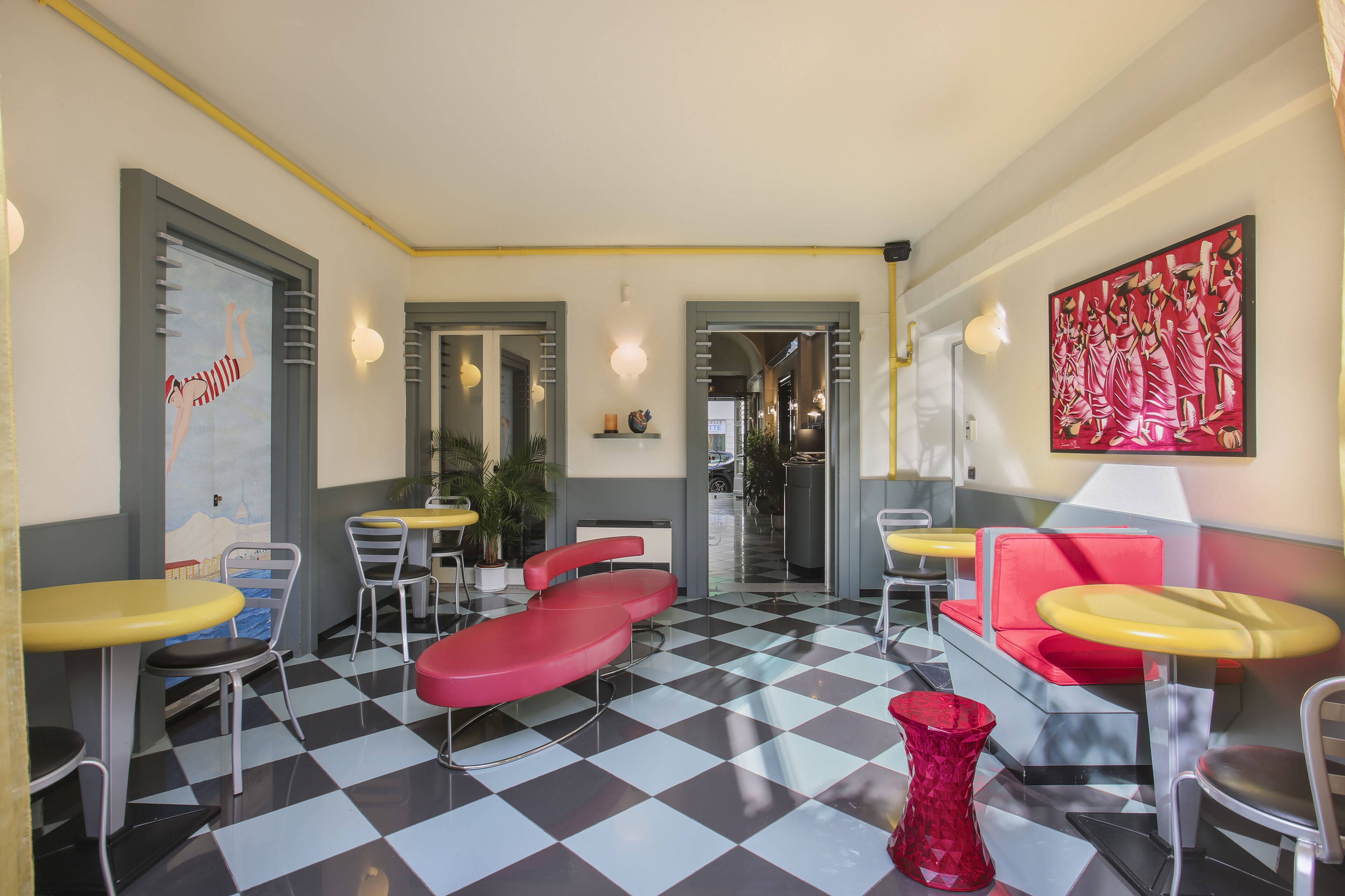 Una cafetería con suelo a cuadros, mesas rojas y amarillas, y una obra de arte roja de gran tamaño en la pared.
