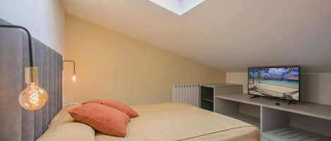 A bedroom with a bed, a TV on a stand, a skylight, and a radiator.