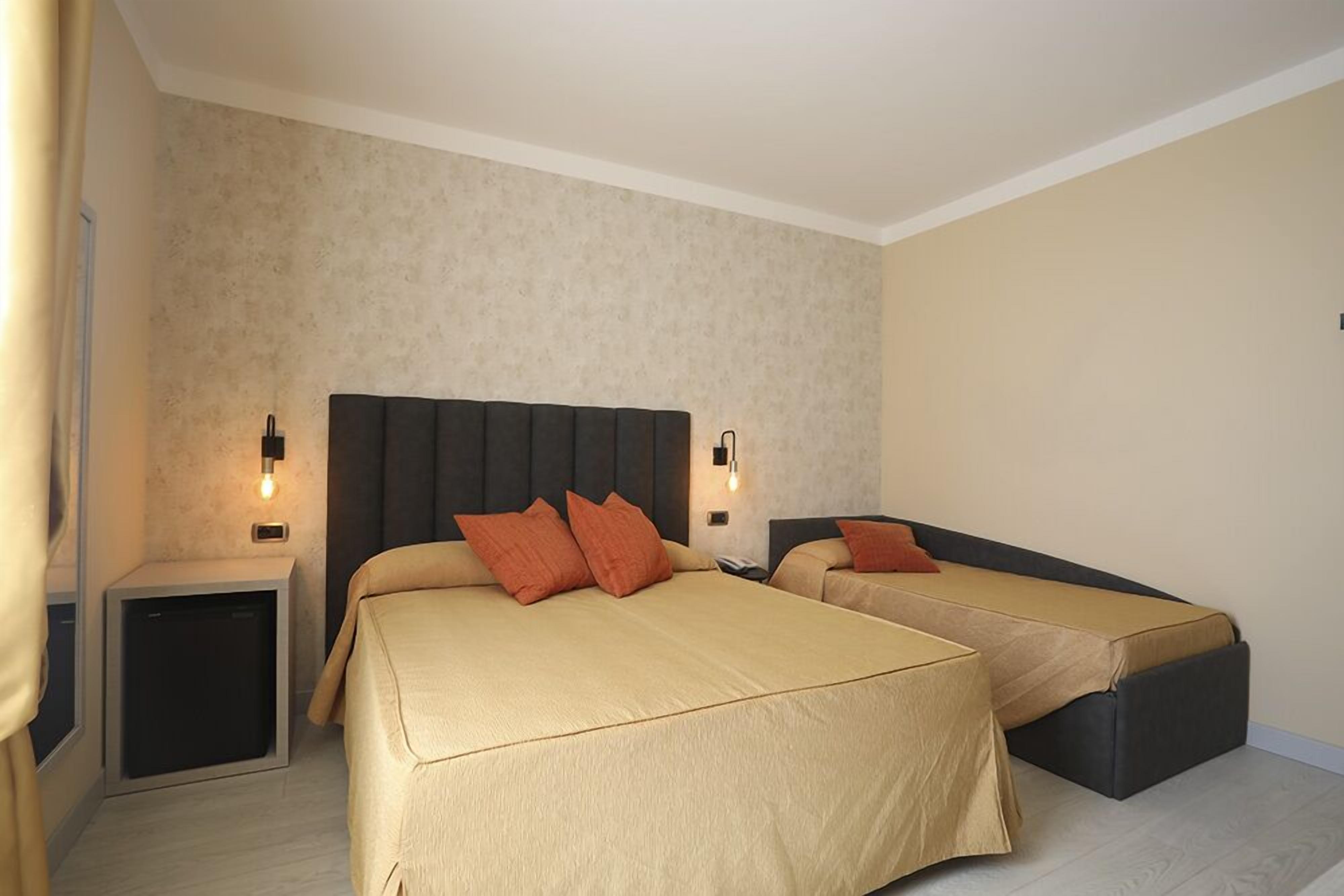 A hotel room with two beds, a small bedside table, and a wall-mounted light fixture.