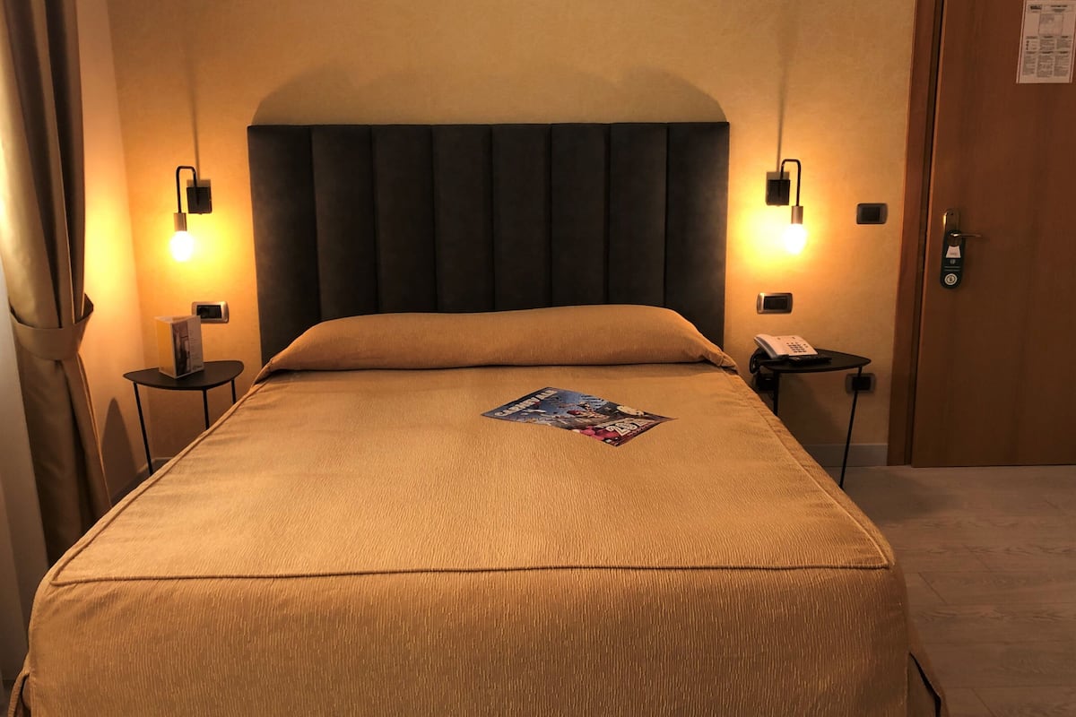 Ein Hotelzimmer mit einem großen Bett, zwei Nachttischen, einer Tür und einer wandmontierten Lampe.
