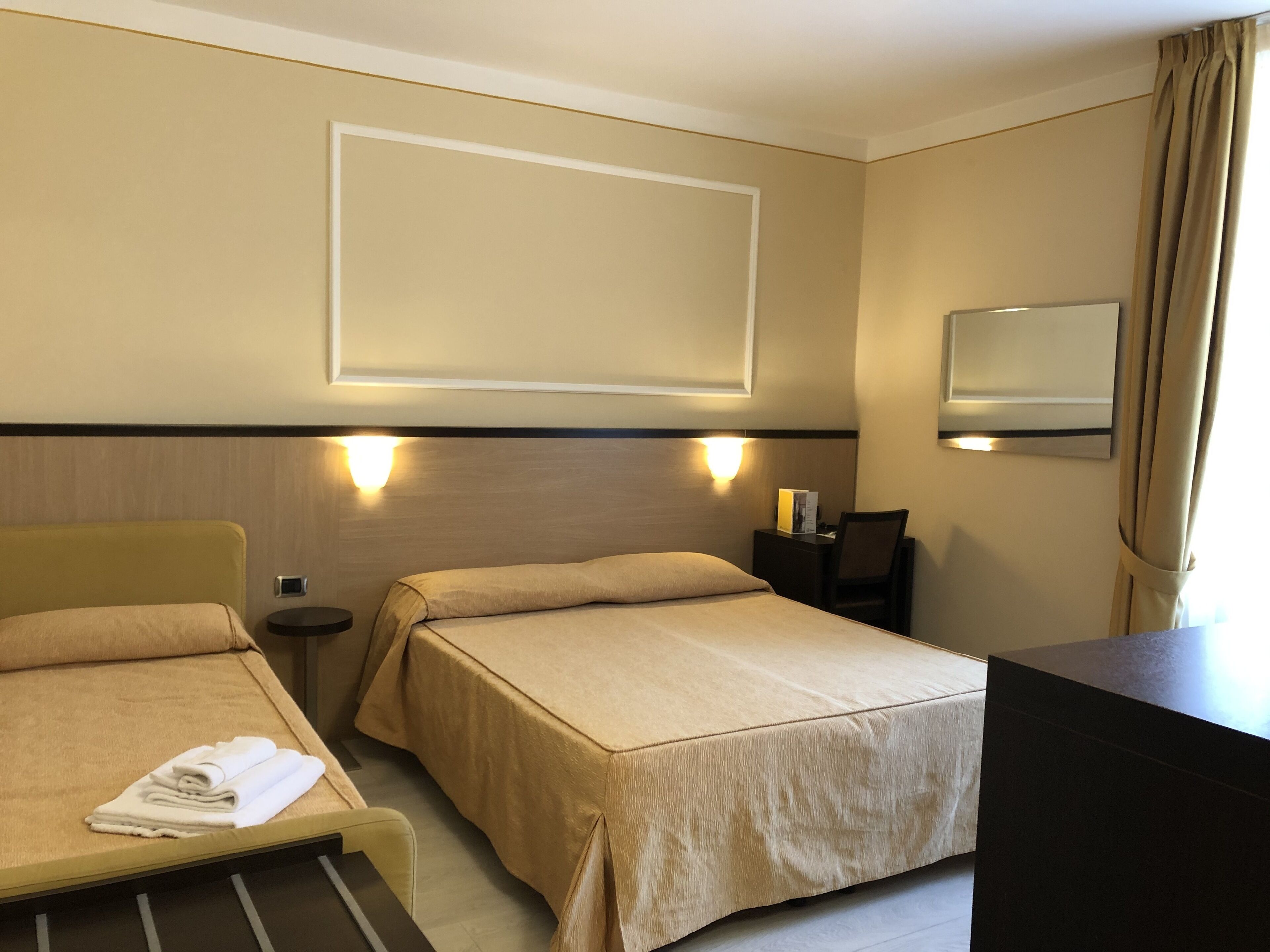 A hotel room with two beds, a desk, a chair, and a large mirror.