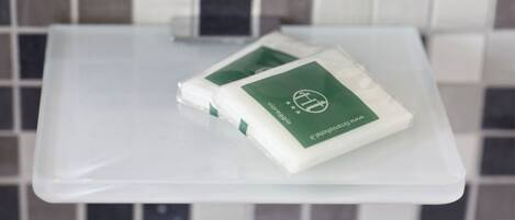 Dos paquetes blancos con etiquetas verdes sobre una bandeja de plástico transparente frente a una pared de azulejos.