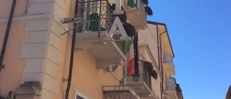 Un edificio de varios pisos con balcones, una puerta visible y un cielo azul claro.