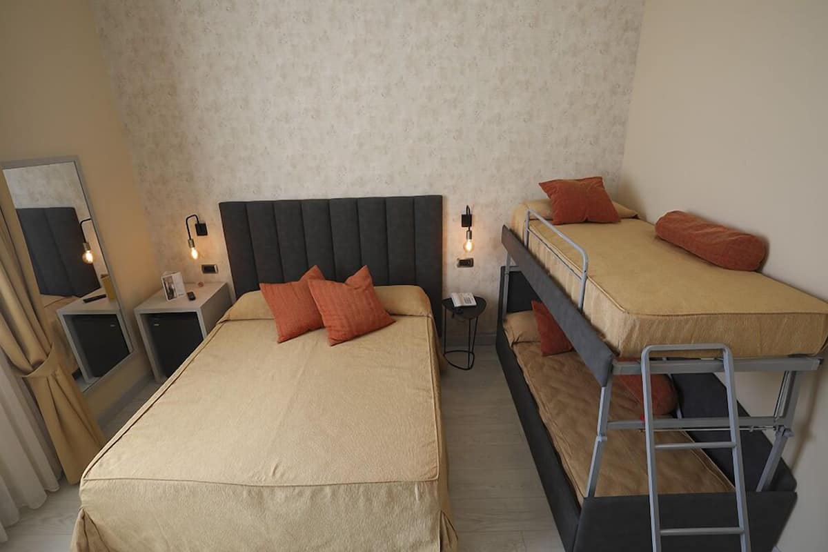 Ein Zimmer mit zwei Betten, eines mit Kopfteil und das andere ein Etagenbett. Nachttische mit Lampen und ein kleiner Tisch zwischen den Betten.