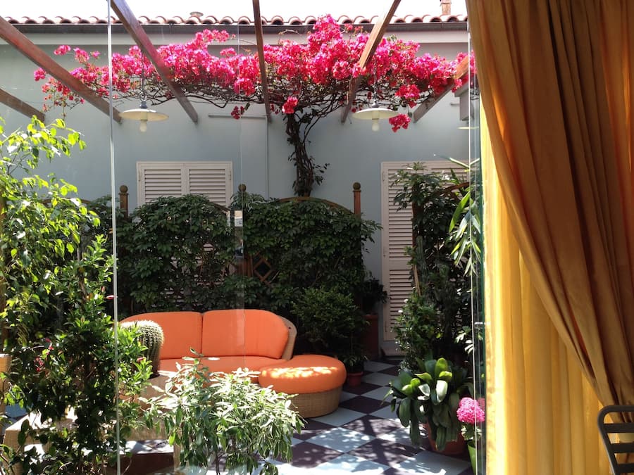 Une terrasse avec un sol à carreaux, un canapé en osier et diverses plantes en pot.