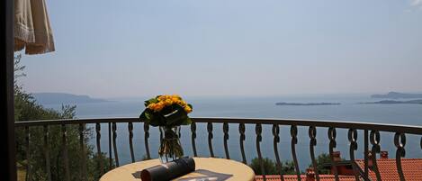 Un balcón con una mesa, un jarrón de flores y vista al mar.