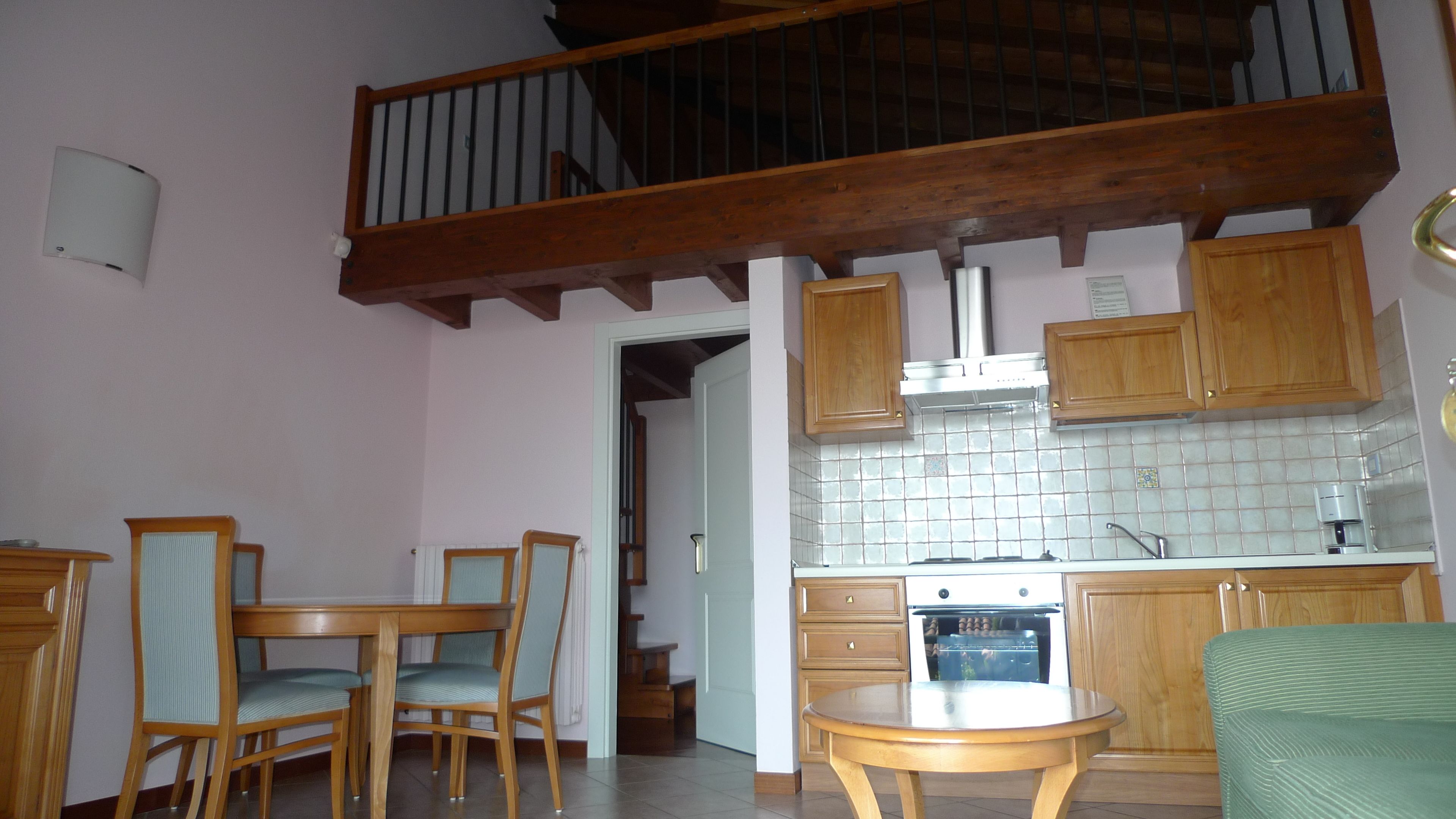 Cuina amb armaris de fusta, un frontissó de rajola i una cuina. Hi ha una zona de dinar amb taula i cadires.