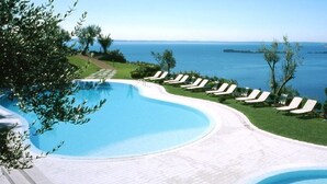Une piscine à bordures courbes, entourée de chaises longues et de parasols, donnant sur une étendue d’eau.