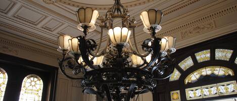 An ornate chandelier with multiple light fixtures, a detailed ceiling with decorative moldings, and large stained glass windows.