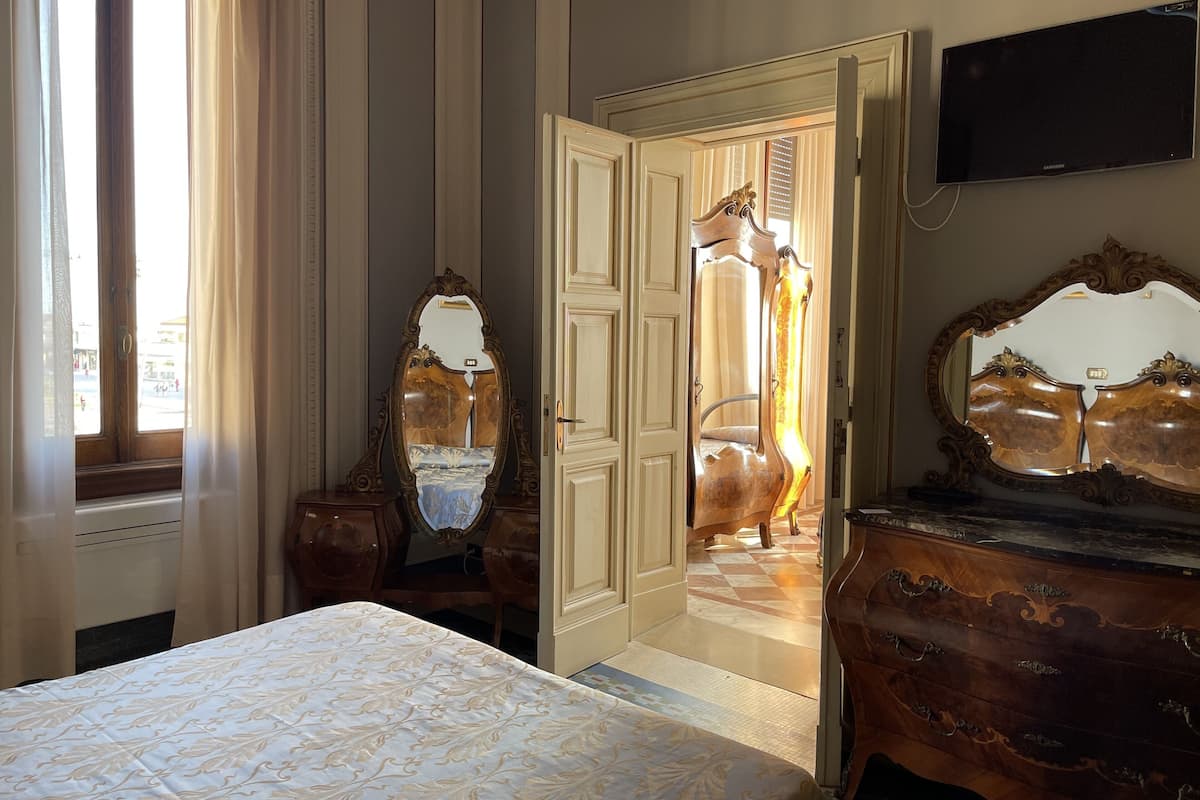 A hotel room with a bed, two ornate mirrors, a dresser, and a television on the wall.