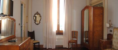 A bedroom with a bed, a wooden dresser, a chair, a wardrobe, a mirror, and a television.
