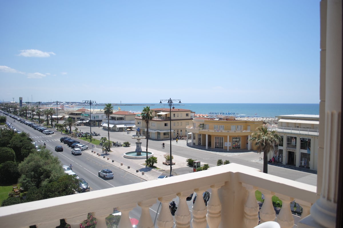 A coastal cityscape with a view of the sea, a busy street with cars, and buildings with balconies.