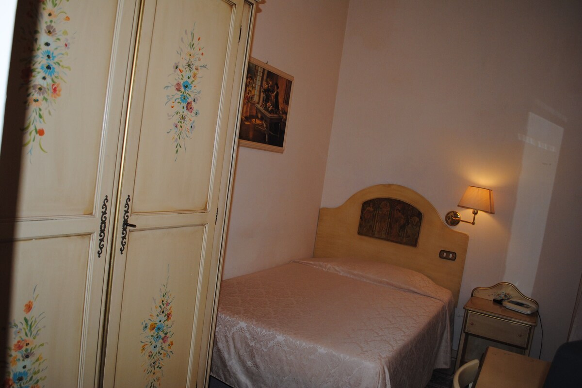 A bedroom with a bed, a nightstand, a lamp, and a wardrobe with floral designs.