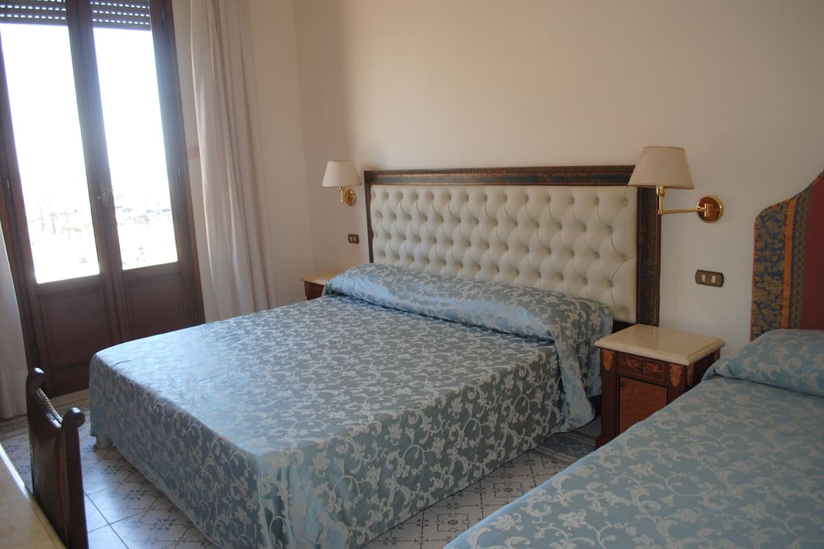 A hotel room with a large bed, two bedside tables, and a window with curtains.