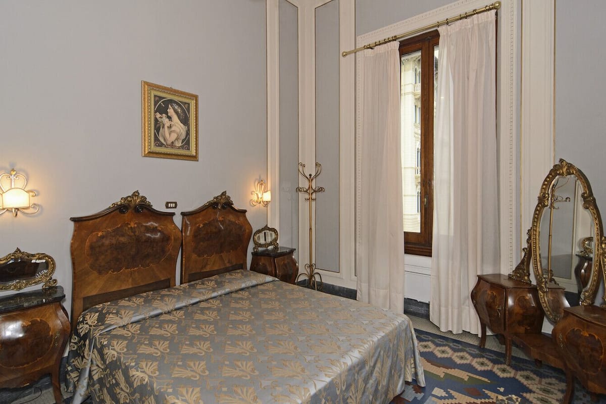 A classic hotel room with a large bed, ornate wooden headboard, a mirror, and a picture on the wall.