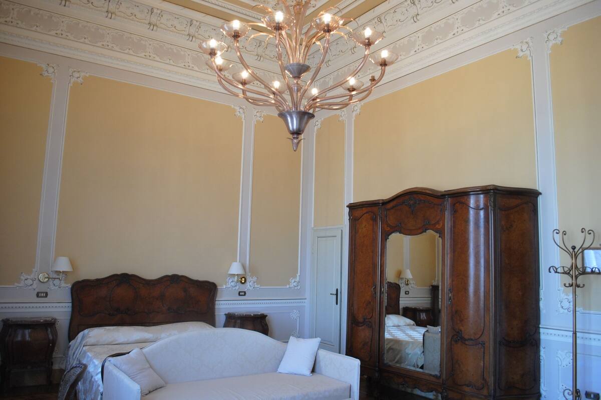 A classic room with a large bed, ornate ceiling, and a wooden wardrobe.
