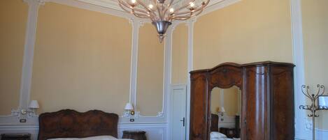 A classic room with a large bed, ornate ceiling, and a wooden wardrobe.