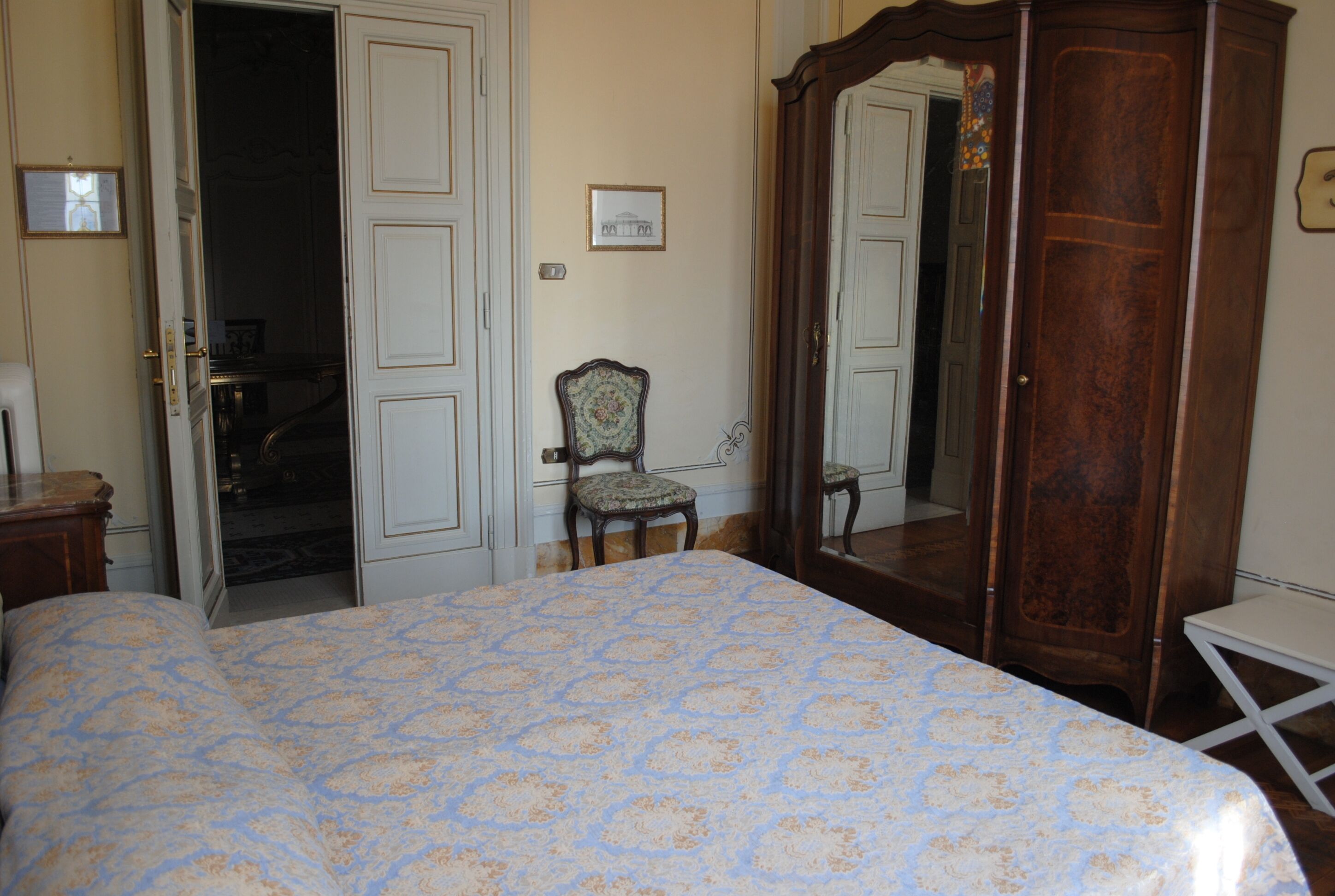 Ein Schlafzimmer mit einem Bett, einem Holzschrank, einem Sessel und einer Tür zu einem anderen Raum.