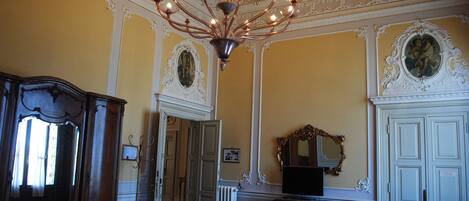 Una habitación con candelabro, decoraciones ornamentales en las paredes, un espejo y un aparador de madera.
