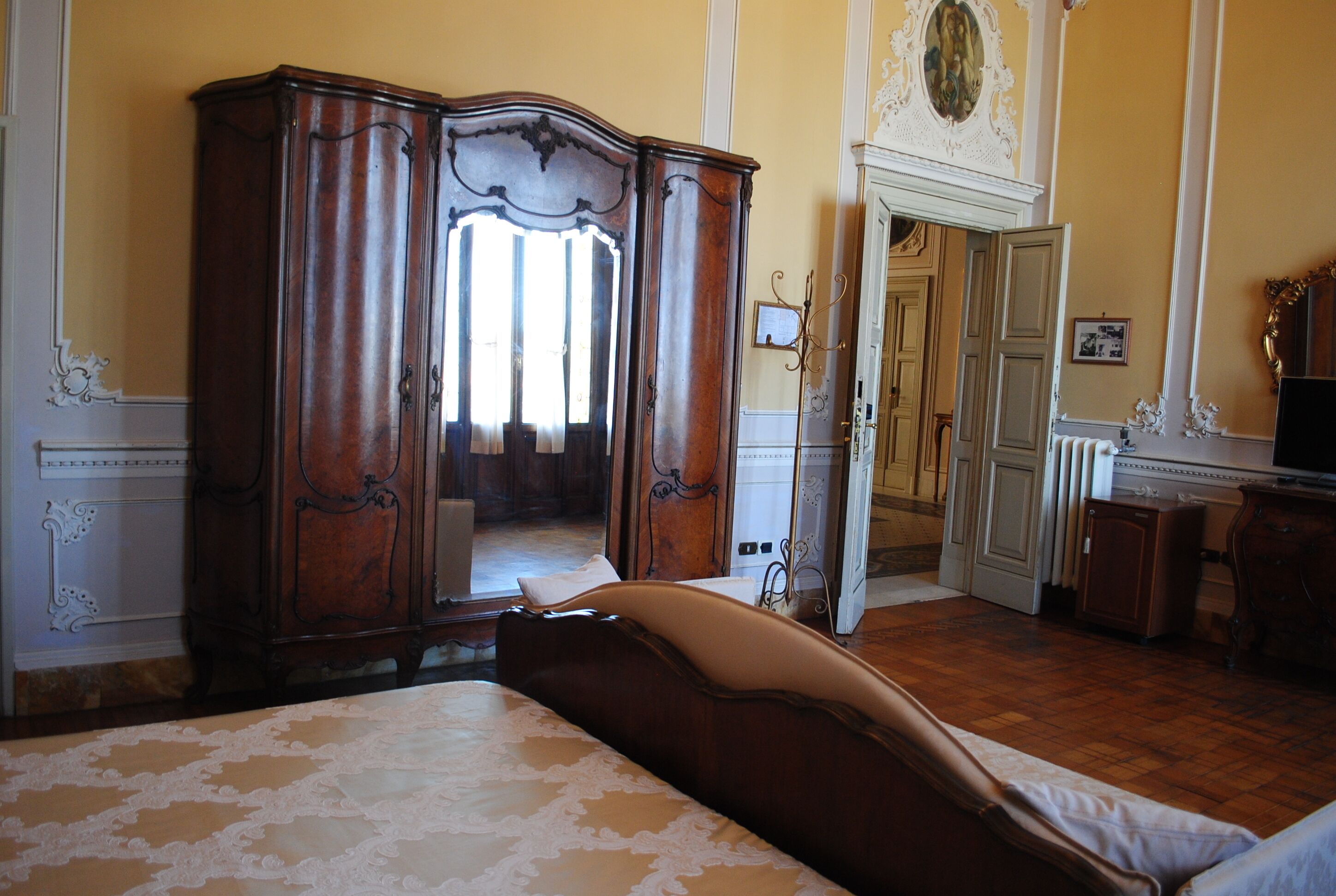 A bedroom with a large bed, a wooden wardrobe, and a mirror.