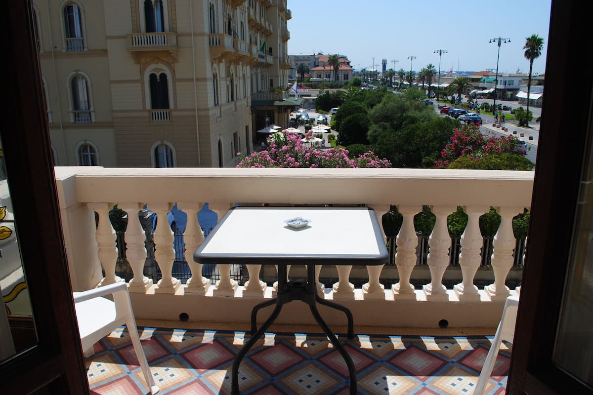 A balcony with a table and chairs, overlooking a street with buildings and parked cars.
