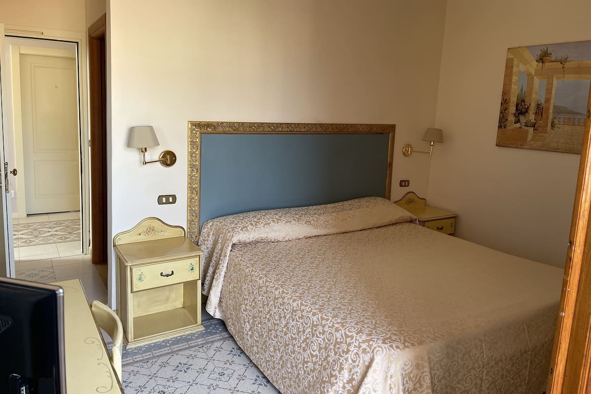 A hotel room with a bed, bedside tables, a desk, and a chair.