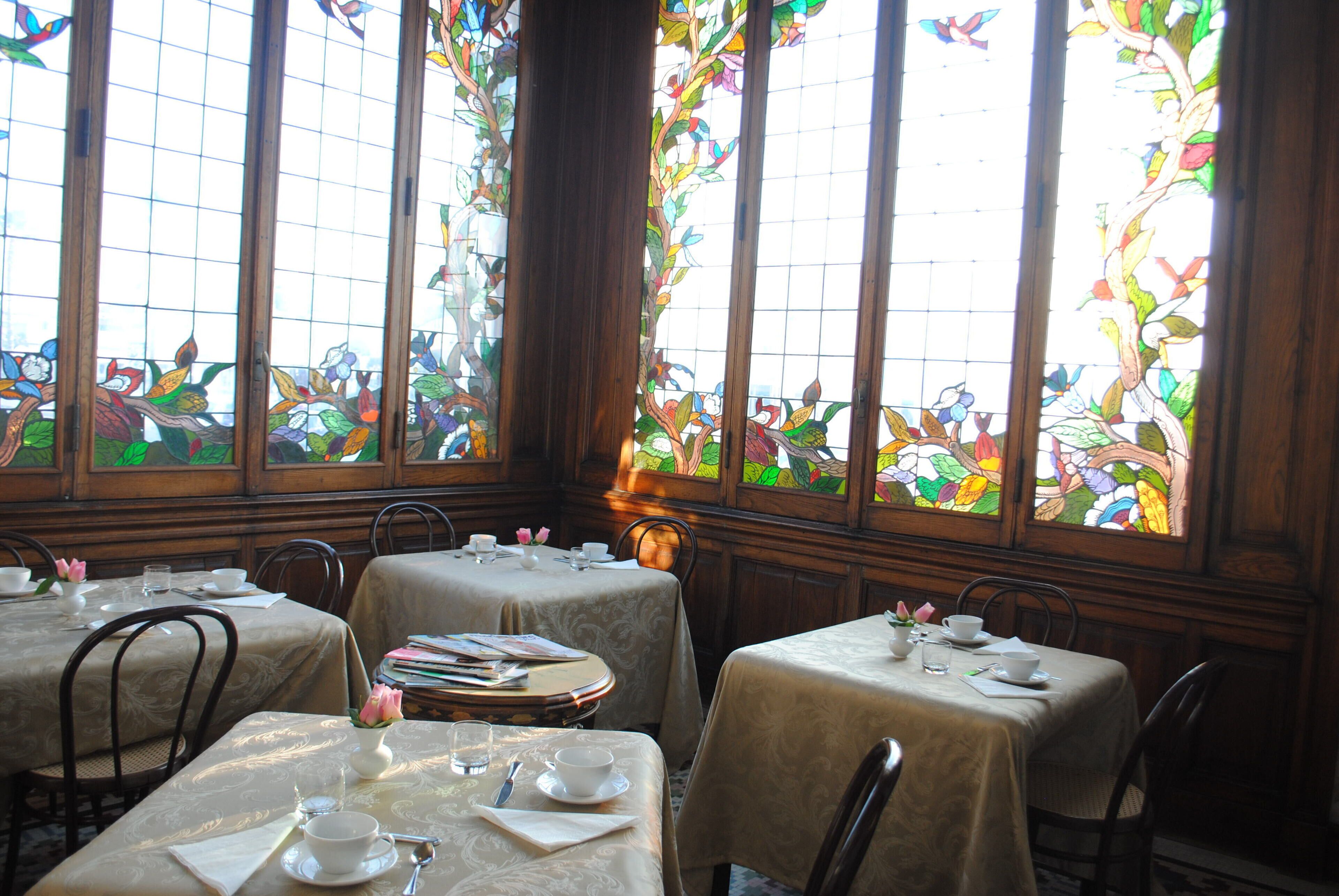 A dining area with tables set for tea service, surrounded by large stained glass windows.