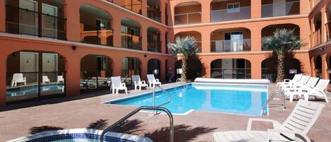 A hotel with a swimming pool, lounge chairs, and a multi-story building with balconies.